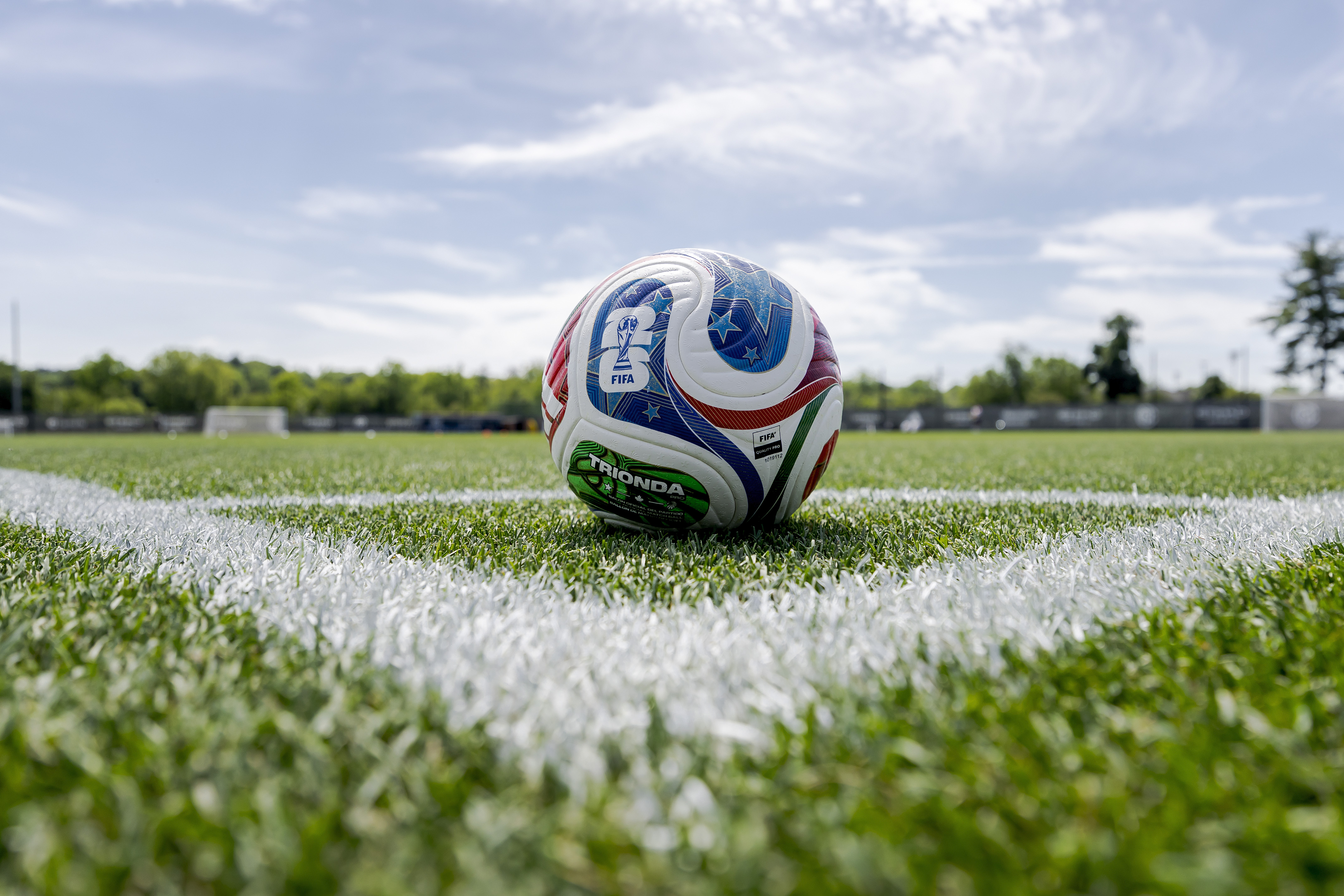 A colorful soccer ball rests on the white corner marking of a vibrant green field.