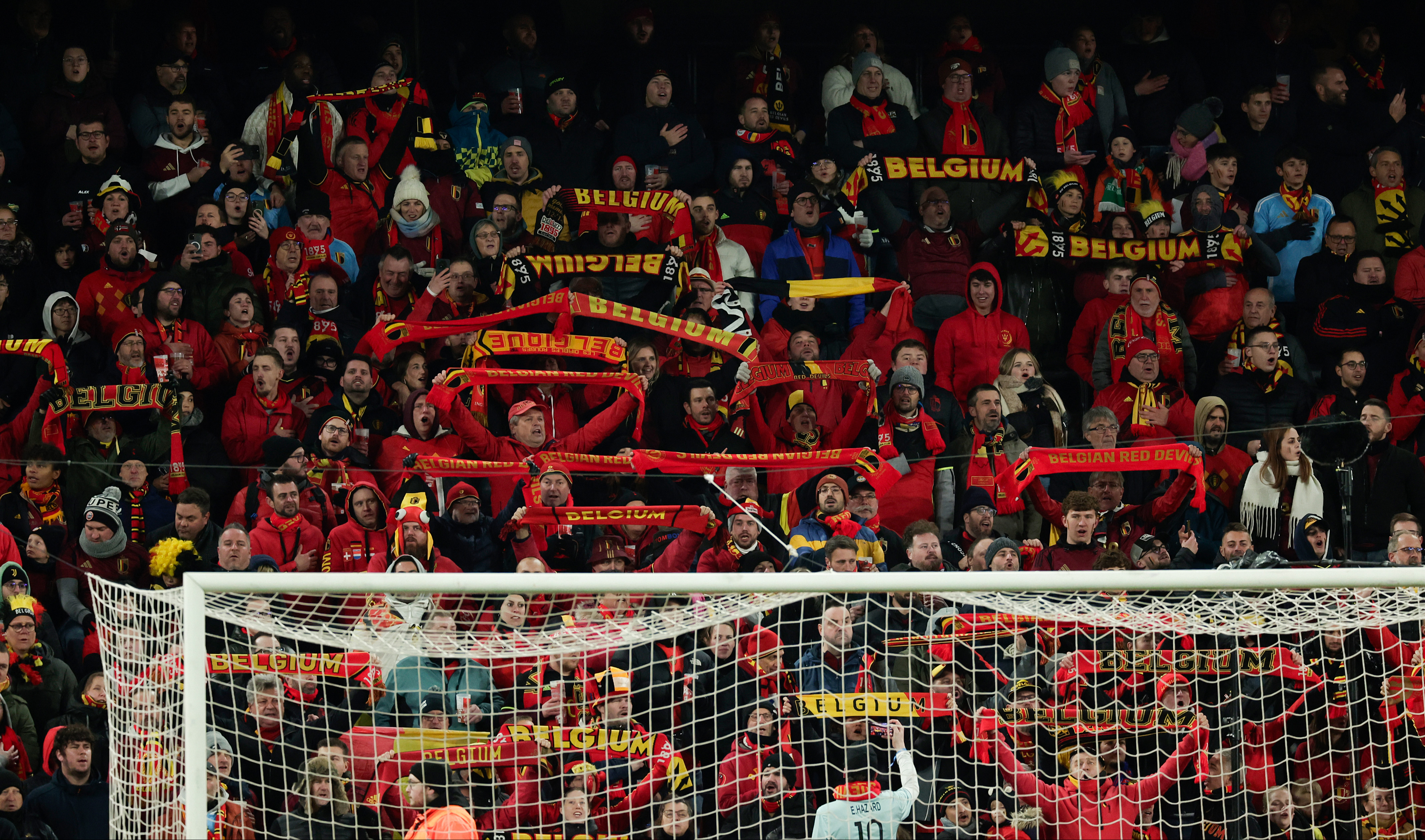 Belgian football fans in red and black cheer behind a goal net.