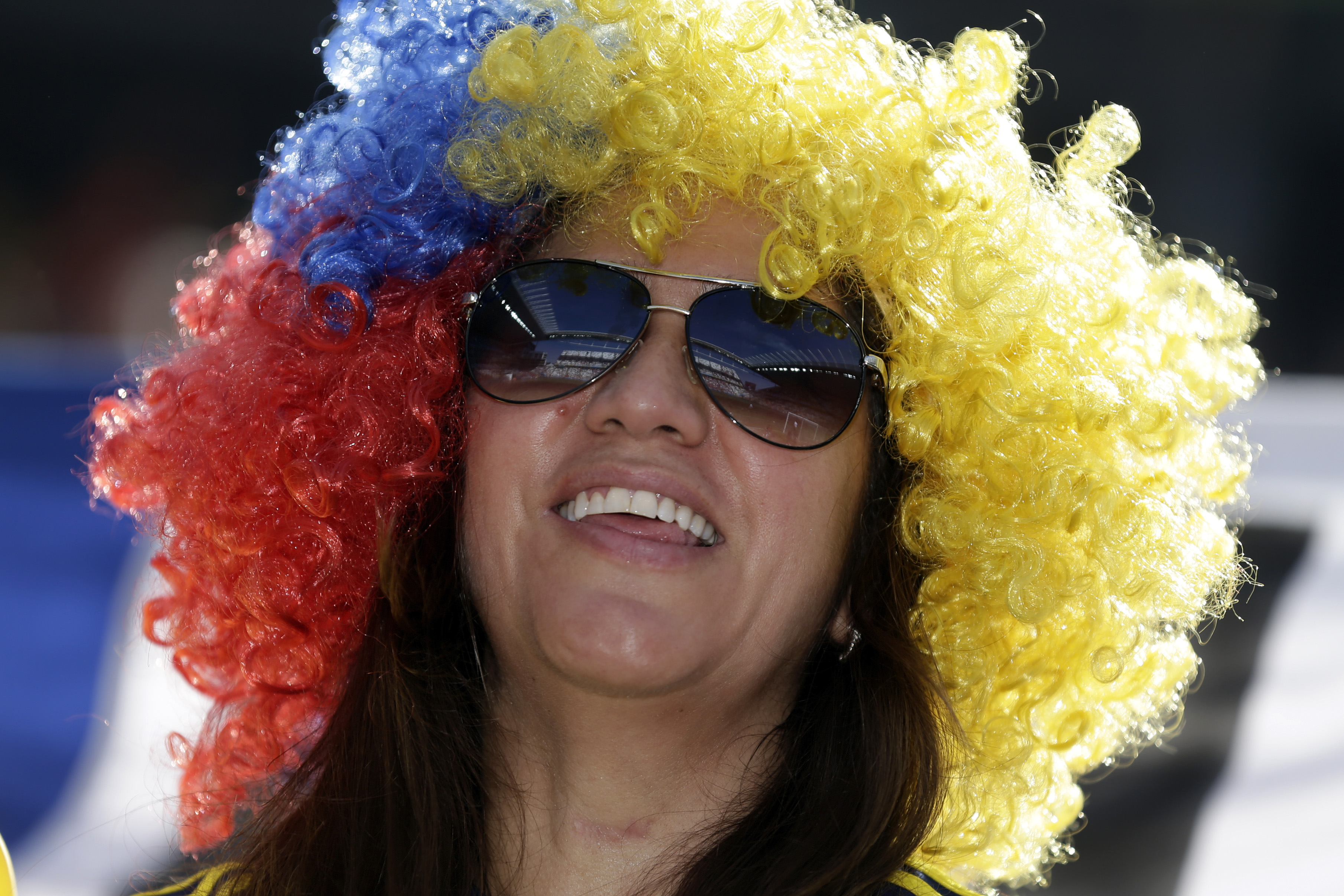 Smiling woman wearing sunglasses and a colorful wig in red, blue, and yellow.