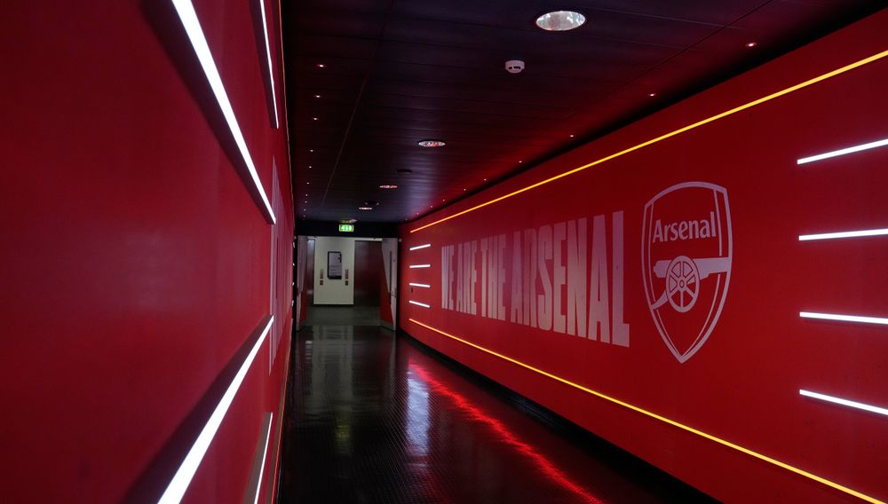 Arsenal FC logo glows in a red, neon-lit hallway with "WE ARE ARSENAL" text.