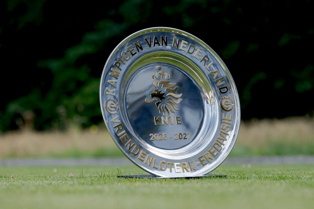 Silver trophy plate with intricate engravings resting on green golf course grass.