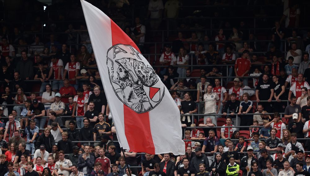 Red and white flag with a black and white logo waves over a cheering stadium crowd.
