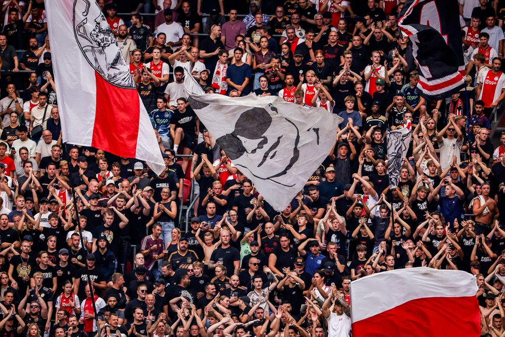 Large crowd of football fans cheering loudly in a stadium with several team flags.