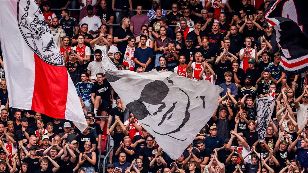 Large crowd of football fans cheering loudly in a stadium with several team flags.