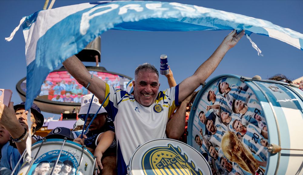Smiling man in striped shirt waves blue and white flag at a celebration.