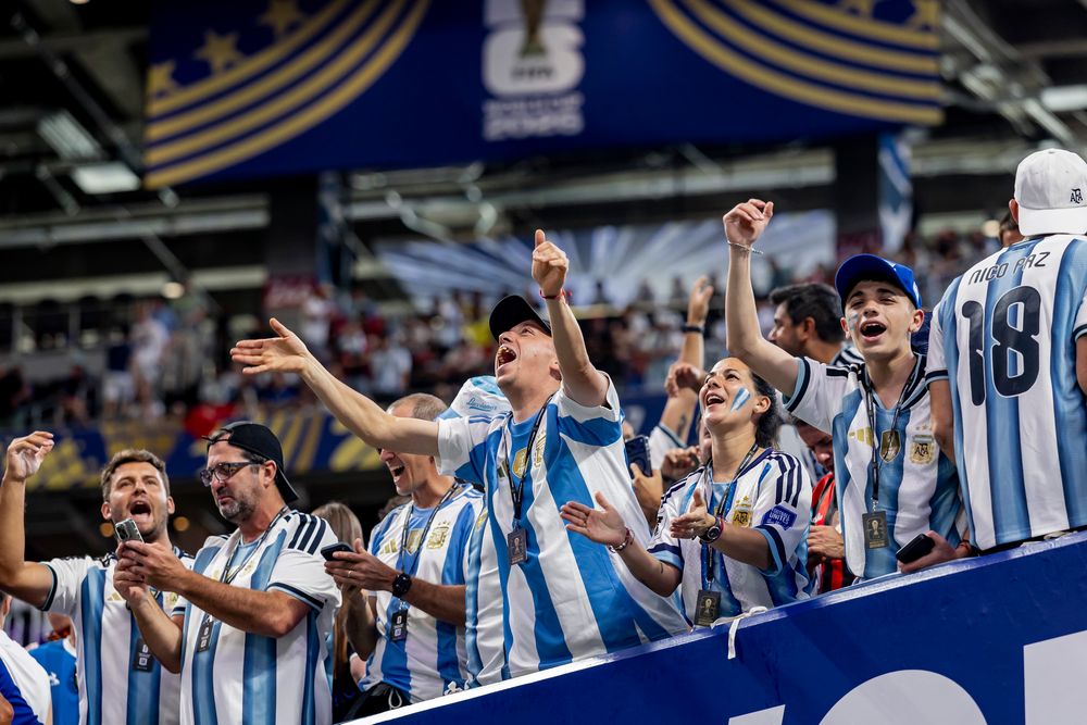 Argentinian football fans cheer enthusiastically in blue and white striped jerseys inside a stadium.