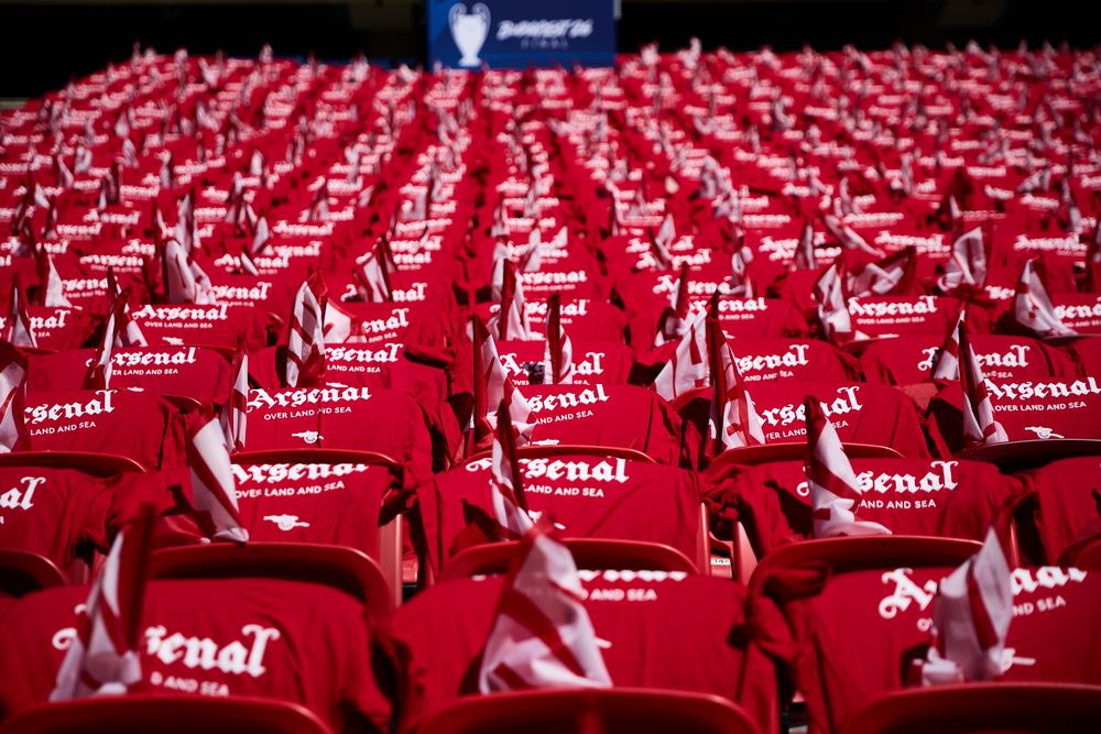 Rows of red Arsenal football shirts fill stadium seats under a Champions League banner.