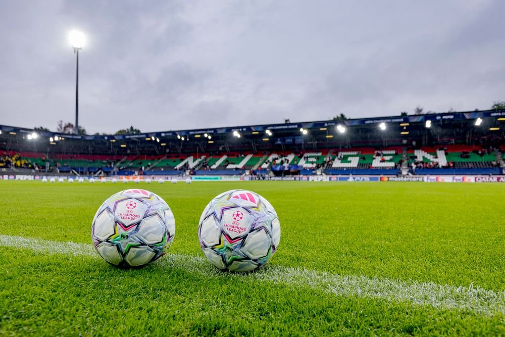 Two soccer balls rest on a green stadium pitch with 'NIJMEGEN' visible on the stands.