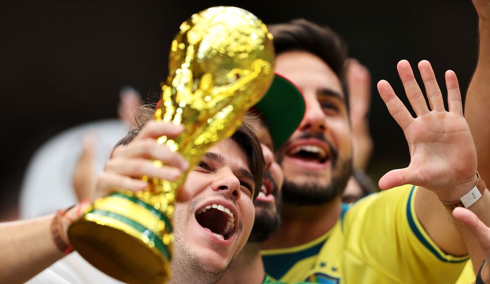 Two excited men celebrate victory, one holding the gleaming golden World Cup trophy.