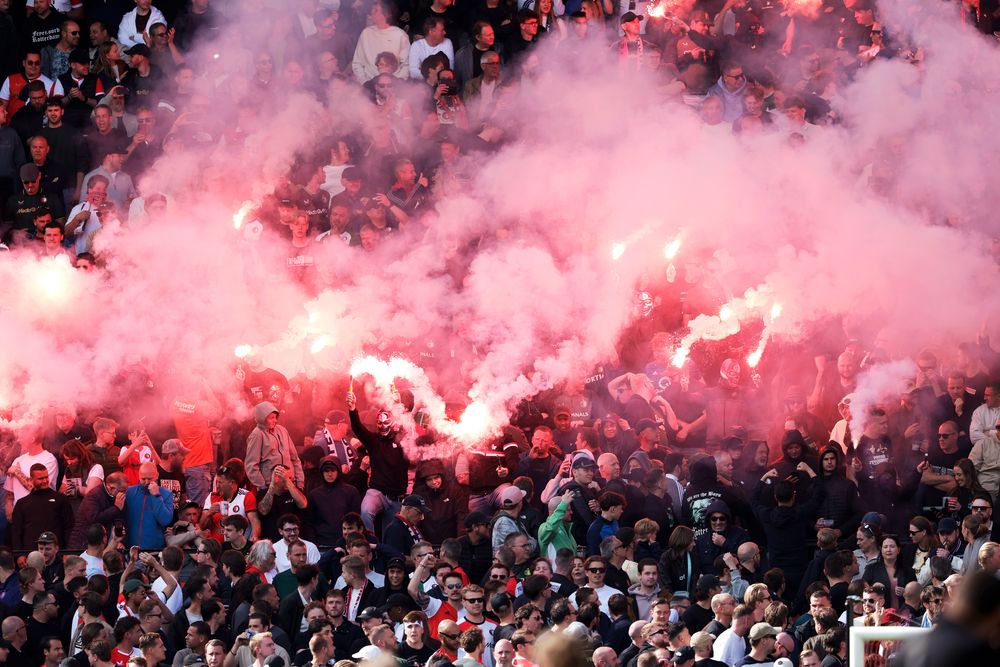 A large crowd of spectators engulfed in thick red smoke from flares.