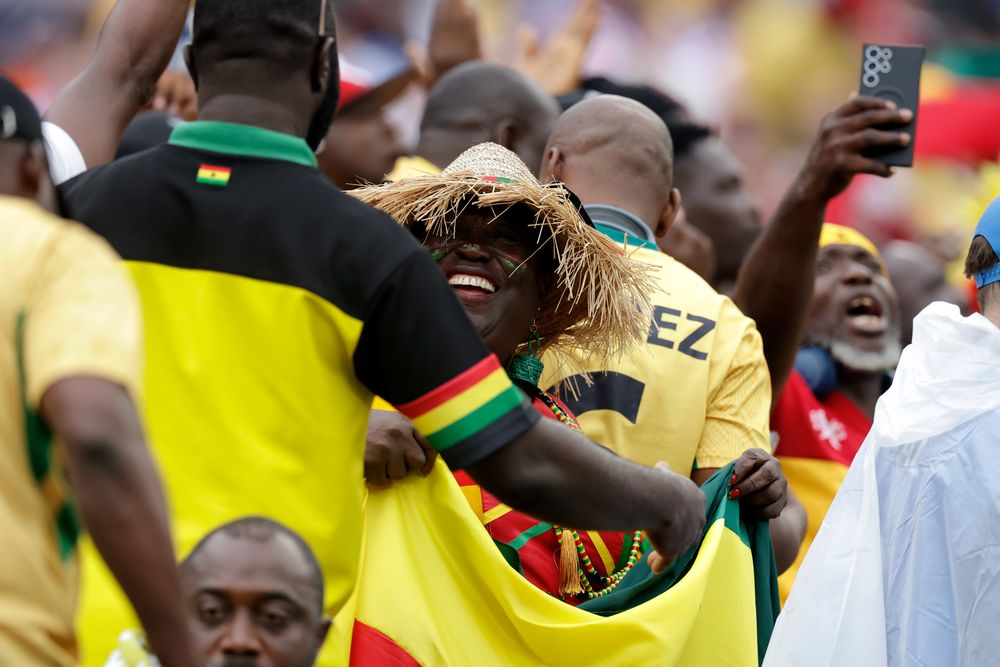 Jubilant soccer fans in yellow shirts celebrate with their national flag, smiling broadly.