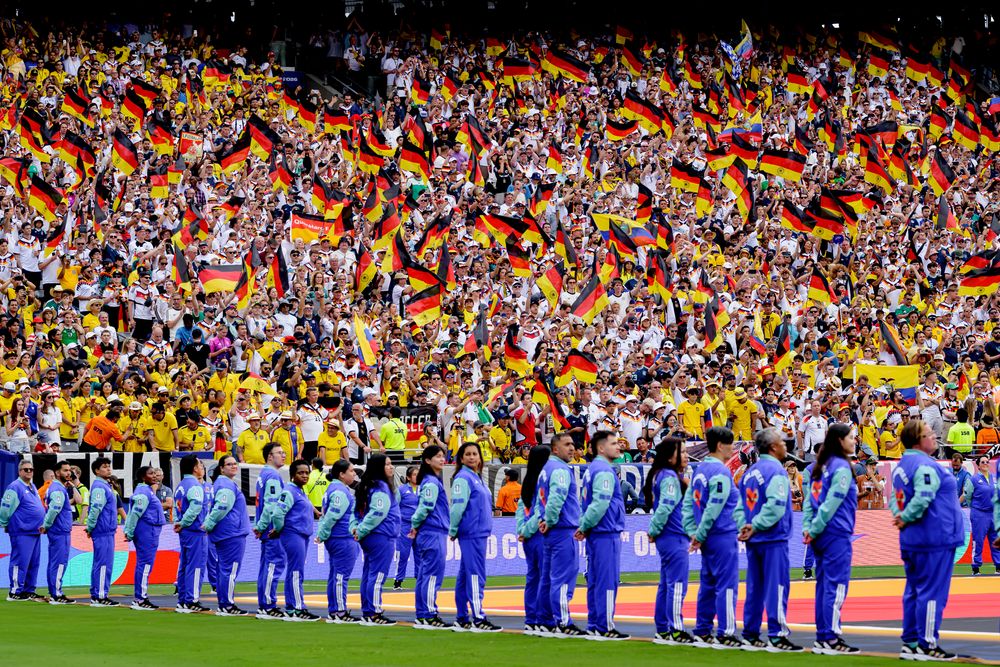 German soccer fans waving flags fill a stadium behind people in blue uniforms.