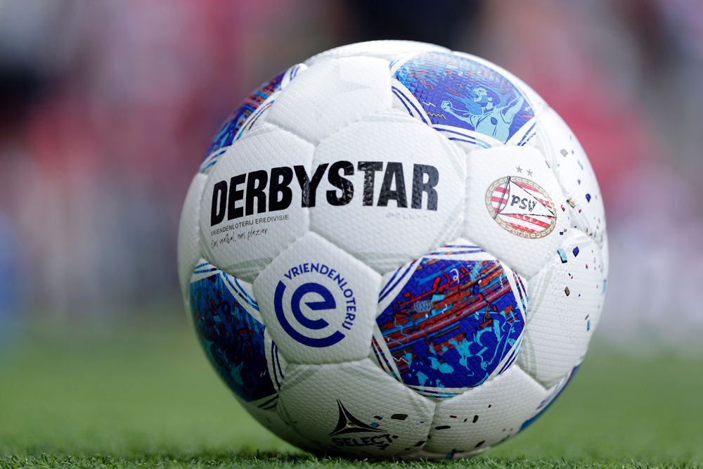White Derbystar Eredivisie soccer ball with blue and red patterns on green grass.