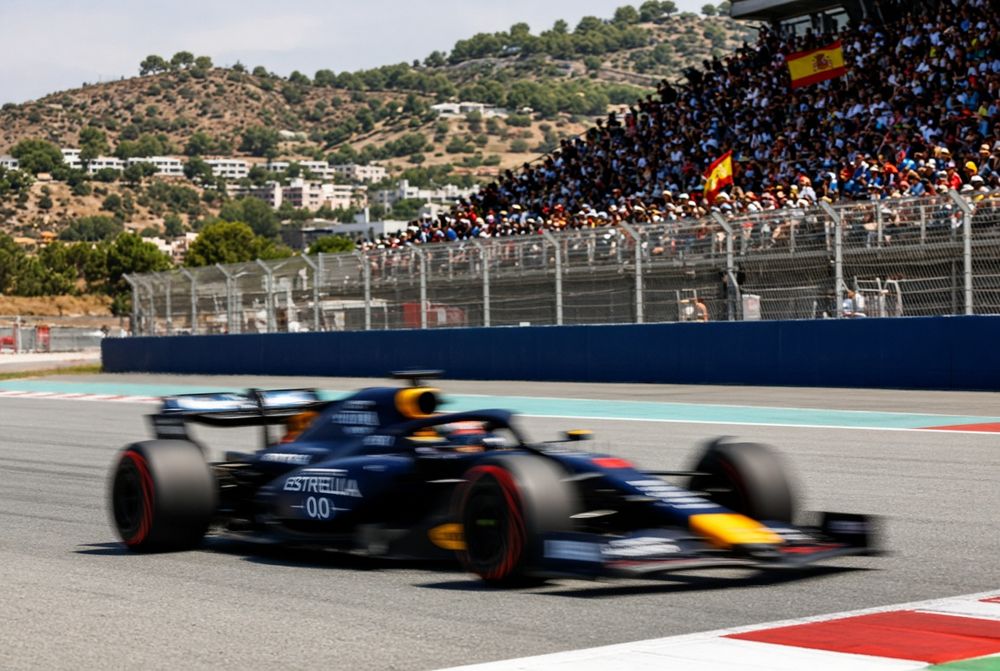 Red Bull F1 car speeds past a grandstand filled with cheering spectators on a sunny race day.