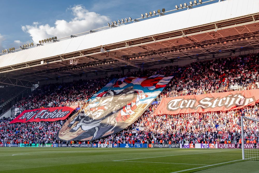 Large tifo banner displaying intricate artwork held by cheering fans in a stadium.