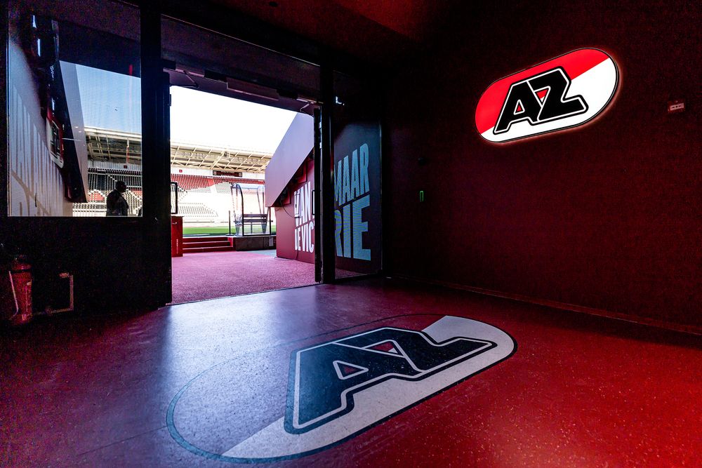 Stadium tunnel with AZ logos on wall and floor, leading to a bright green football field.