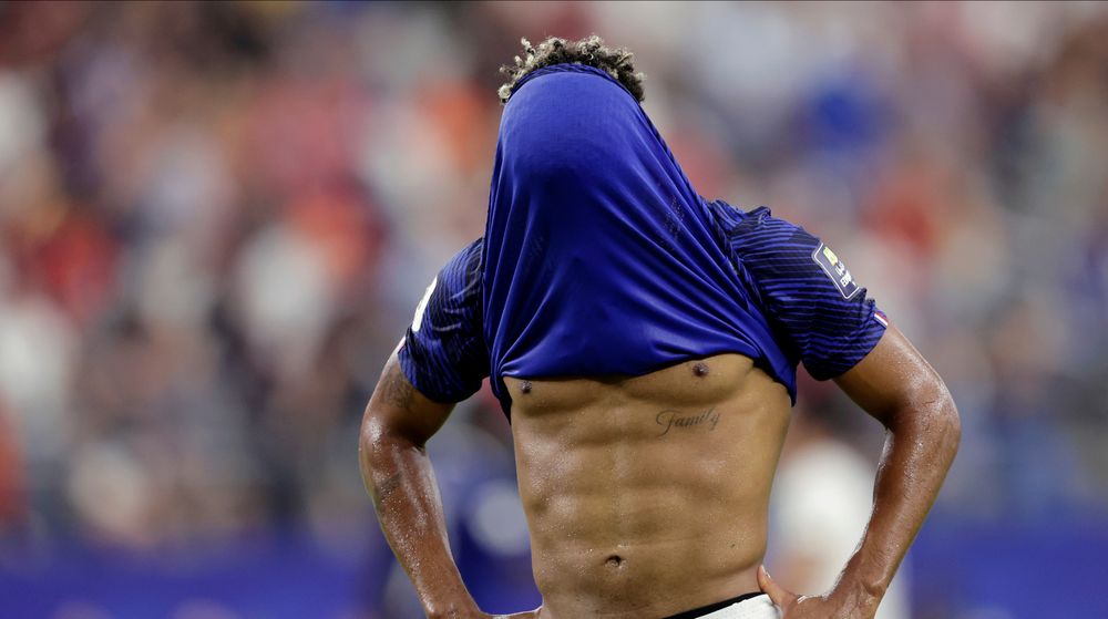 Dejected soccer player with blue jersey pulled over his head, revealing muscular abs.
