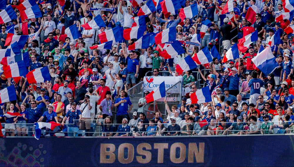 Large crowd of cheering fans waving French flags at a stadium in Boston.
