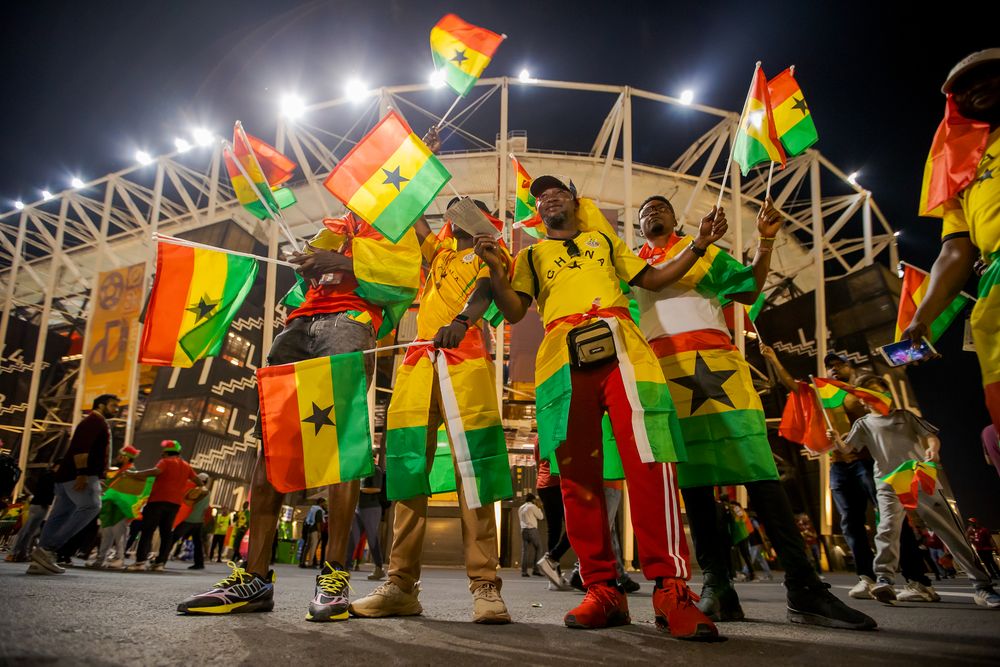 Ghanaian football fans celebrate with flags outside a brightly lit stadium at night.