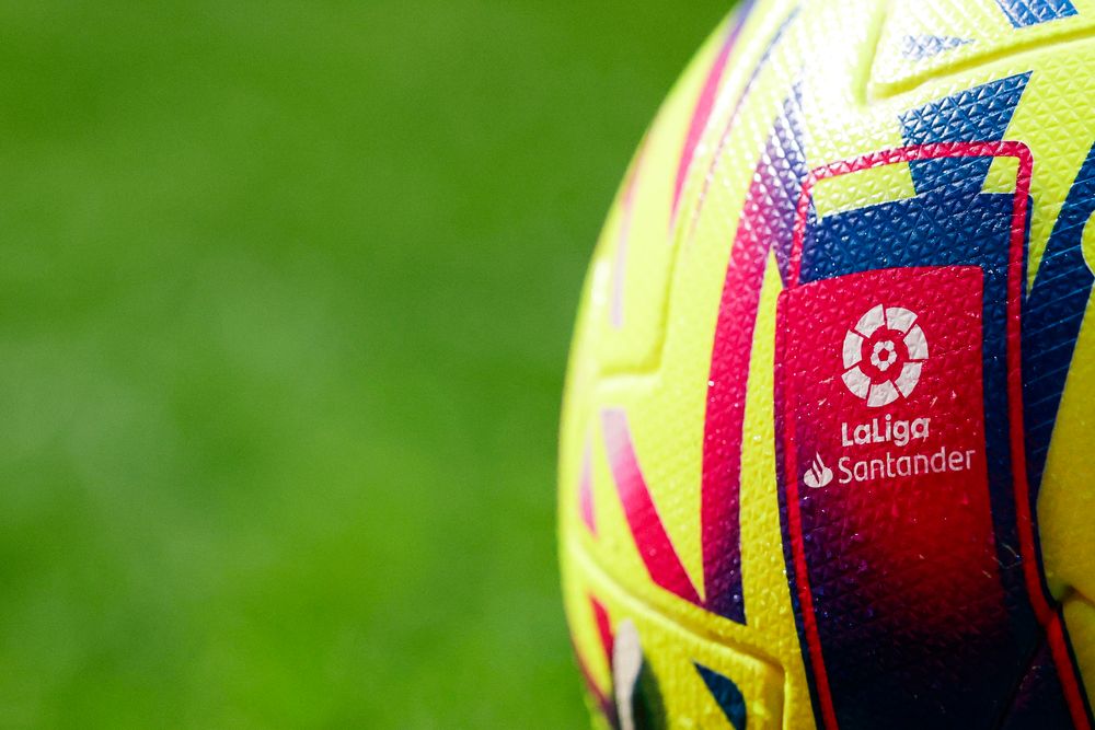A close-up of a yellow and red football featuring the LaLiga Santander logo on a green background.