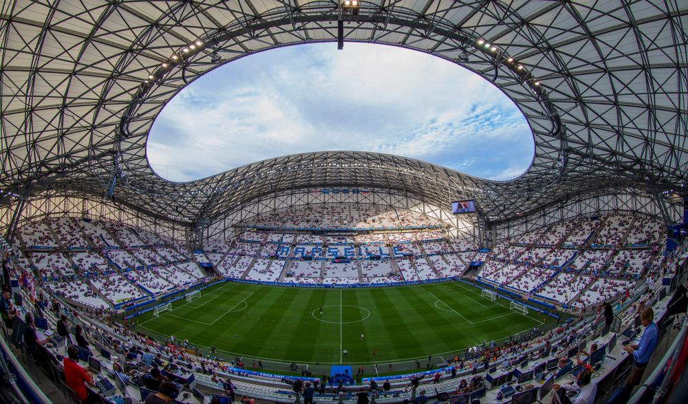 A wide-angle view of a modern football stadium with an open roof and green pitch.