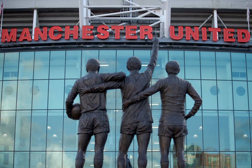 Bronze statue of three footballers in front of the Manchester United stadium.