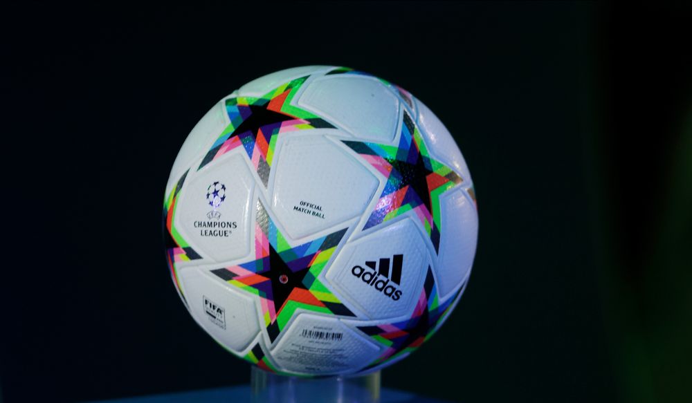 White UEFA Champions League soccer ball with colorful star design and Adidas logo.