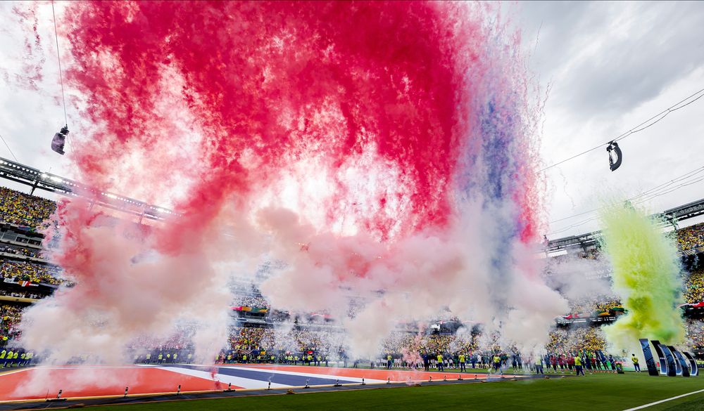 Vibrant red, white, and blue smoke fills a stadium during a celebratory event on the field.