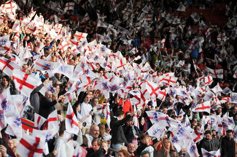 Enthusiastic sports fans wave numerous white and red English flags in a crowded stadium.