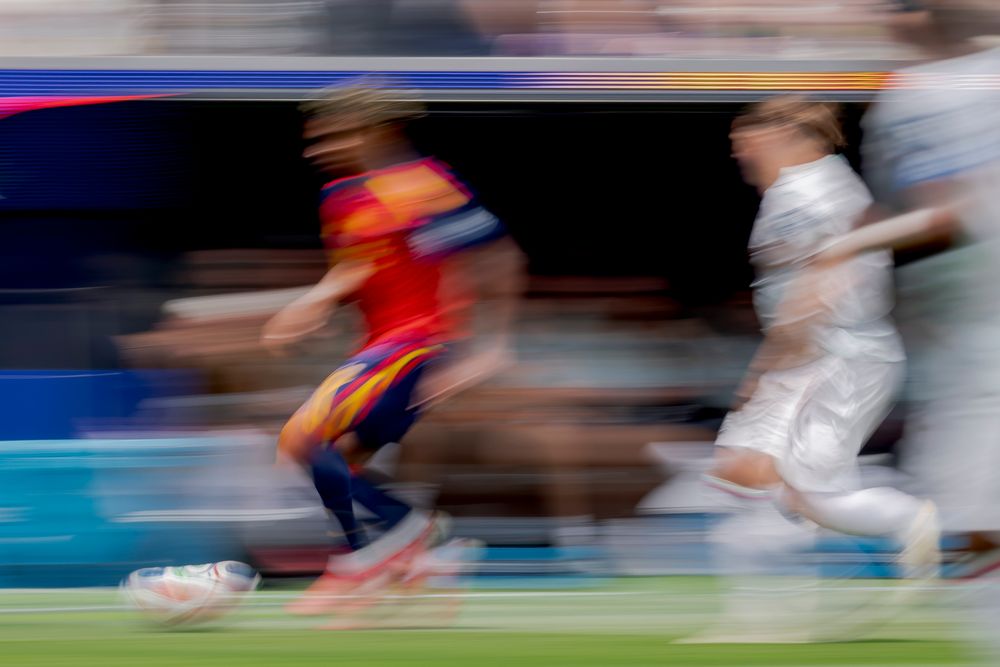 Soccer player in red and yellow dribbles ball with motion blur on field.