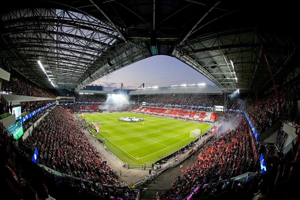 Large sports stadium with a green field, packed stands, and bright lights at dusk.