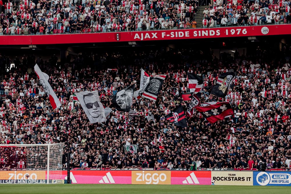 A large crowd of enthusiastic football fans holding flags and banners in a stadium.