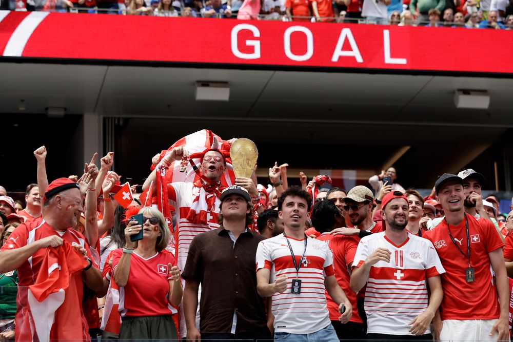Excited soccer fans cheer under a large 'GOAL' sign during a match.