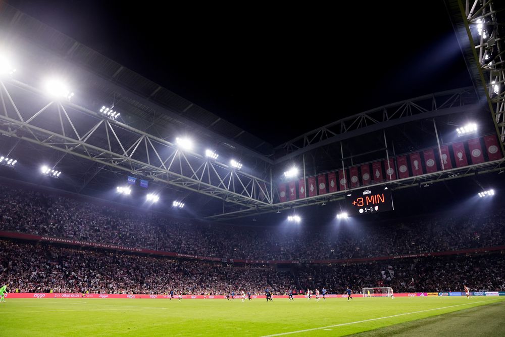 Large football stadium at night, with a packed crowd and bright floodlights illuminating the field.