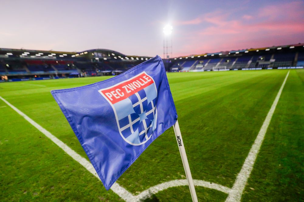 Blue PEC Zwolle corner flag on a vibrant green football pitch at sunset in a stadium.