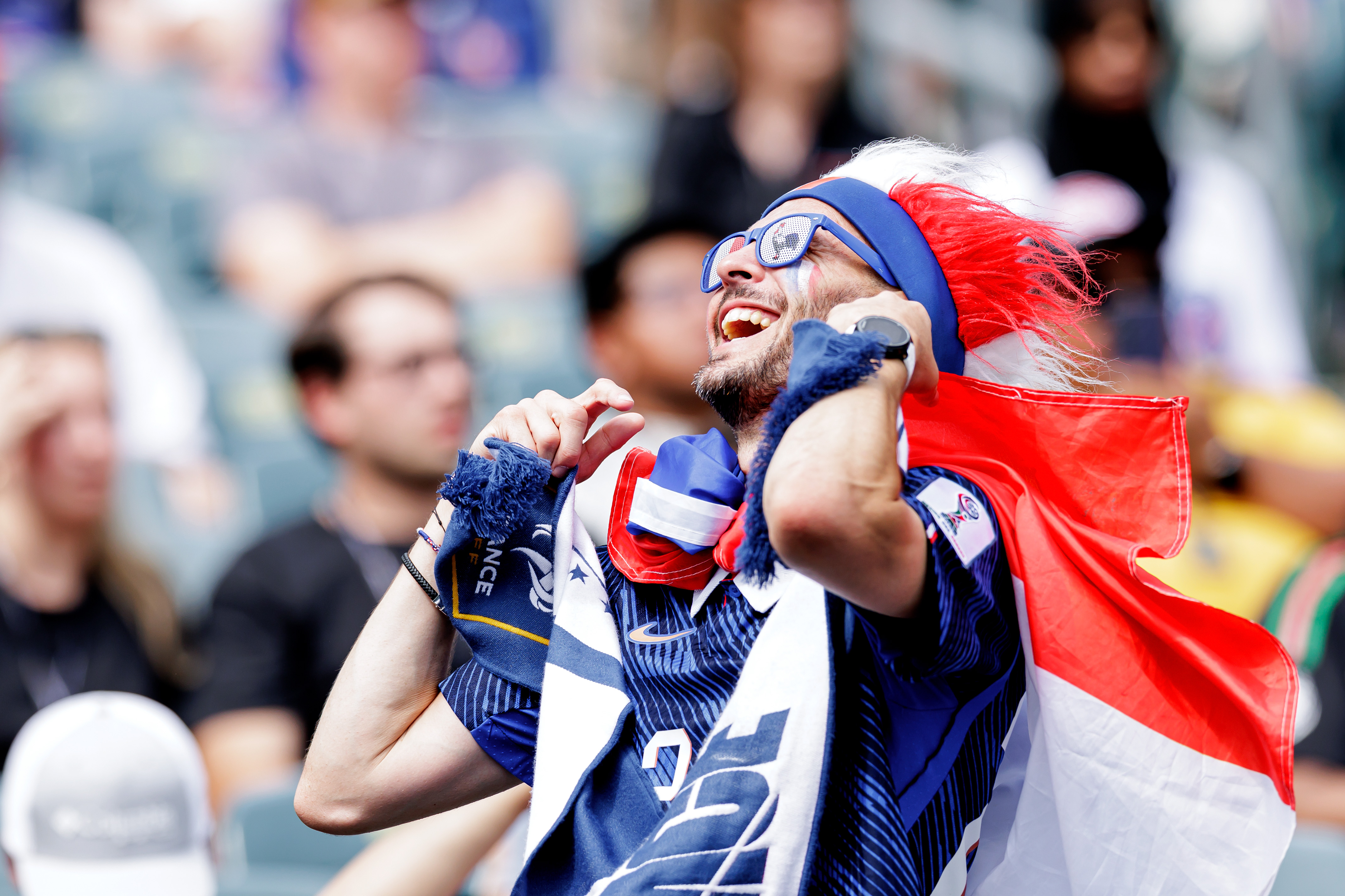 Enthusiastic fan with a French flag and feathered hat cheers excitedly at a sporting event.