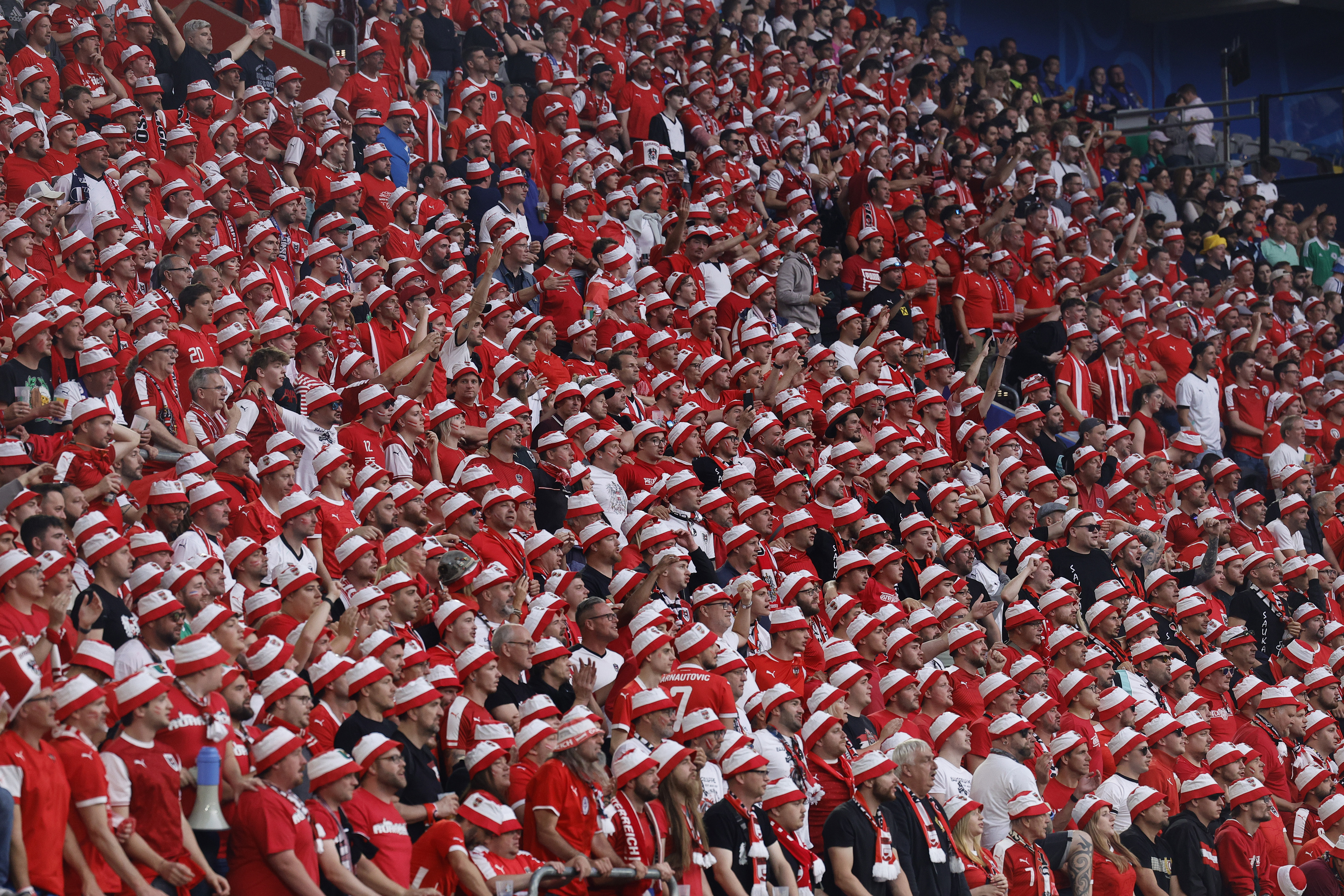 A dense crowd of cheering fans wearing red and white striped hats fills a stadium.