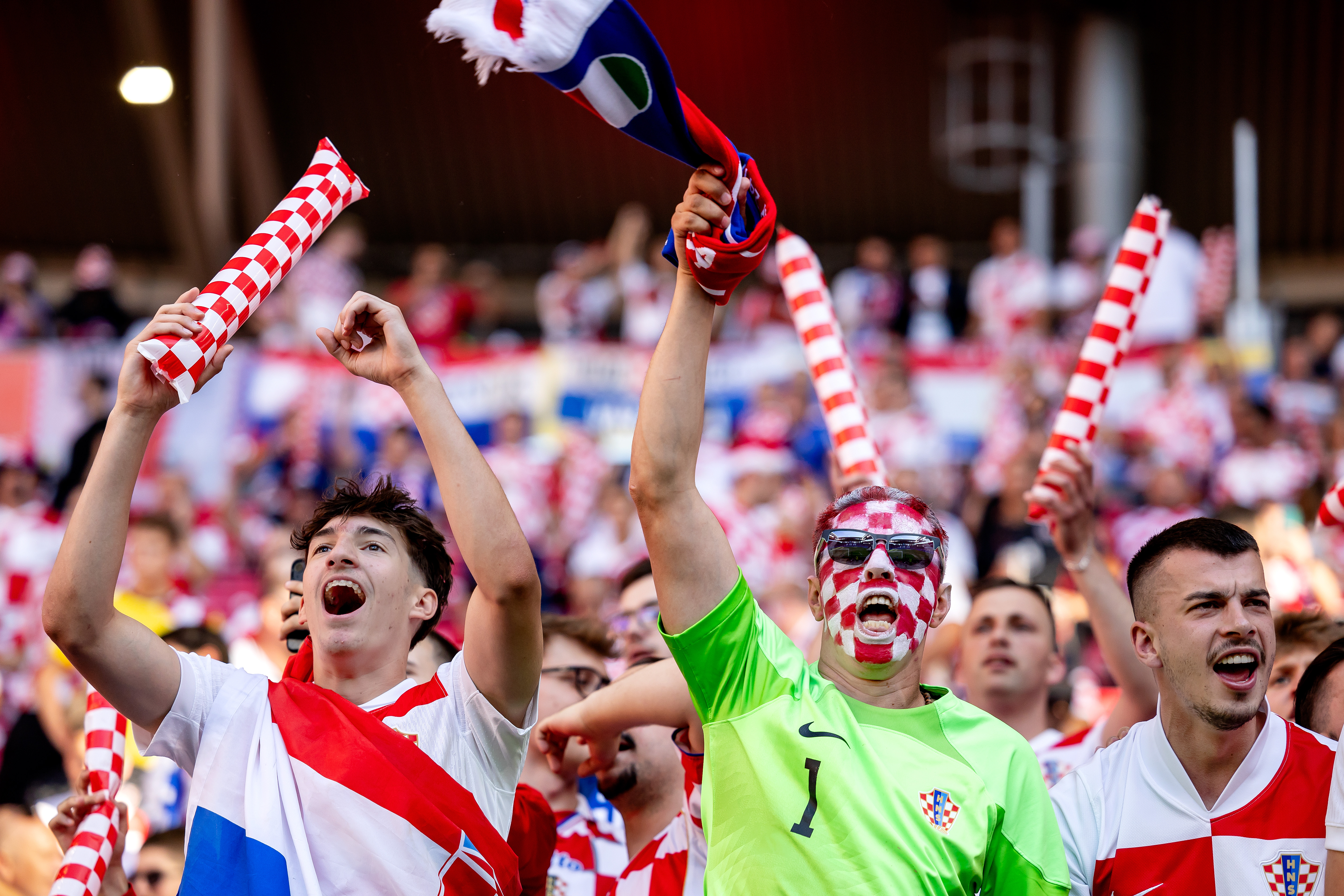 Croatian football fans cheer enthusiastically, waving red and white checkered scarves and flags.