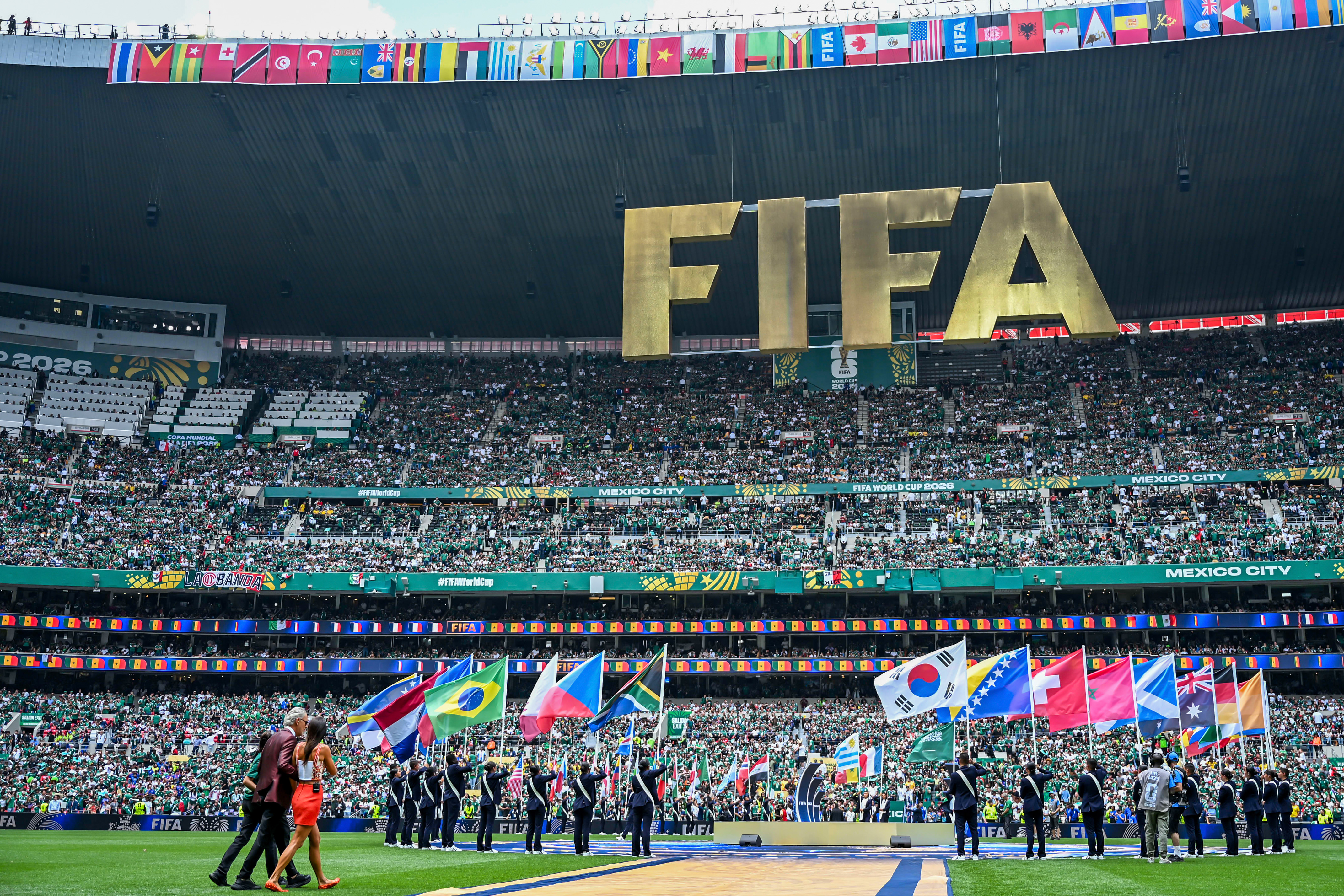 A crowded football stadium with a large golden FIFA logo and flag bearers on the field.
