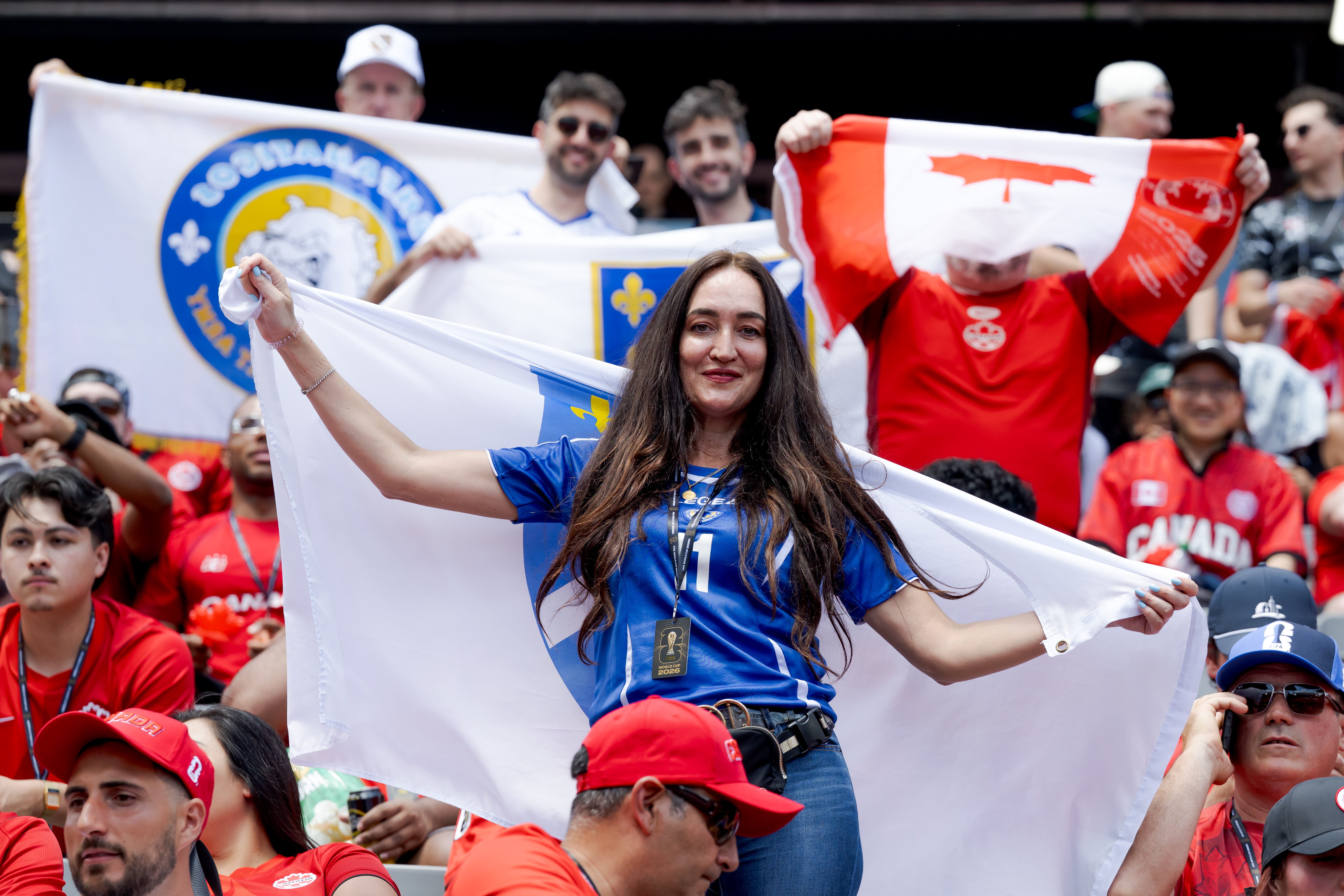 Woman in blue jersey holding a white flag at a lively sporting event crowd.