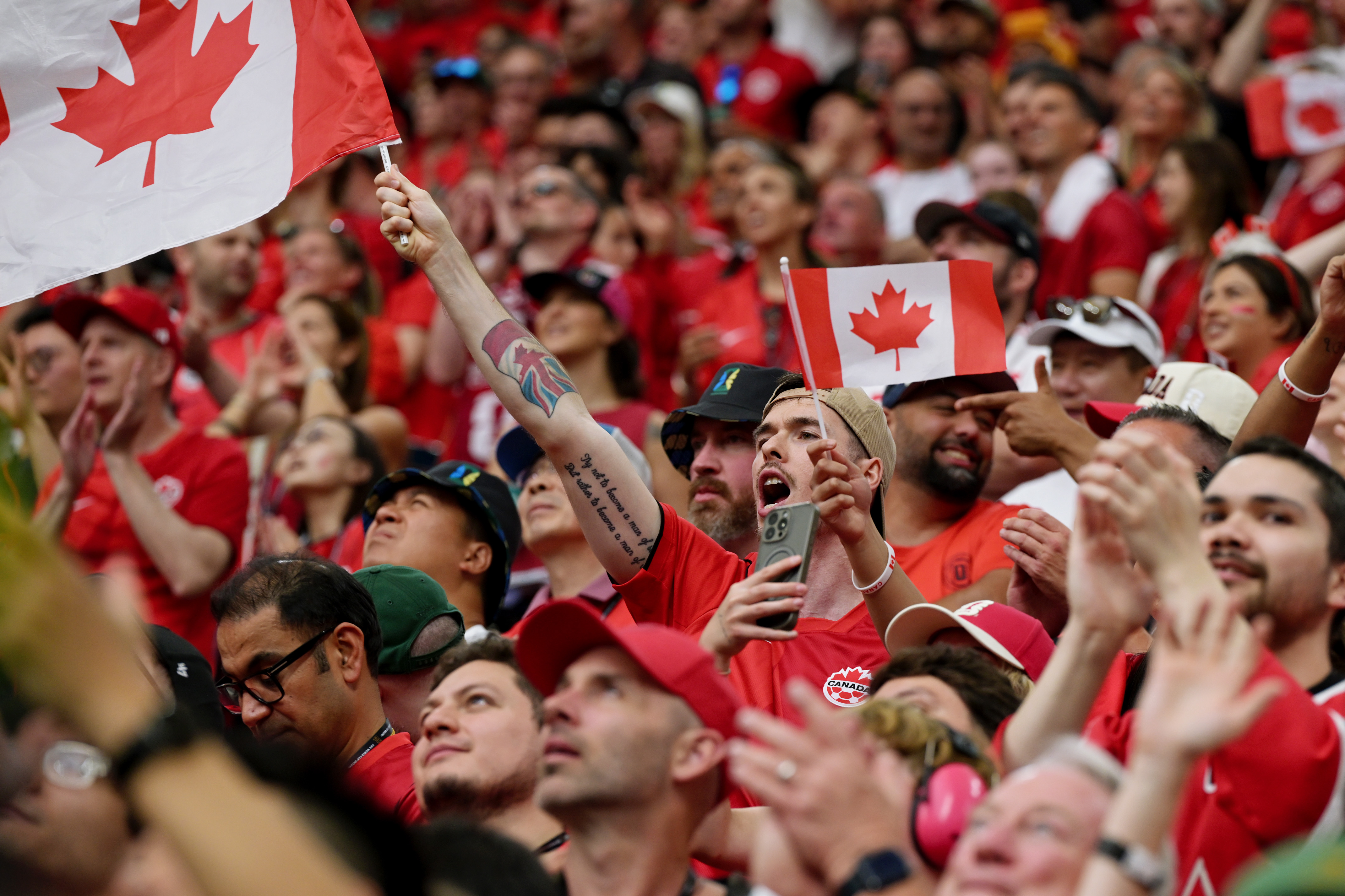 Enthusiastic crowd in red cheers, waving Canadian flags at a sporting event.